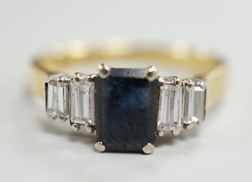 A modern 18ct gold and single stone emerald cut sapphire set ring, with graduated baguette cut diamond set shoulders, size J/K, gross weight 3.1 grams.